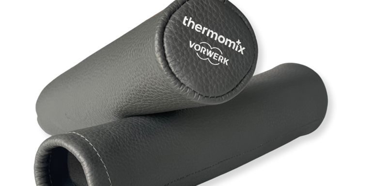 Zwei schwarze Thermomix Griffschützer mit sichtbarer Naht einer zeigt das Thermomix Vorwerk Logo auf der Stirnseite