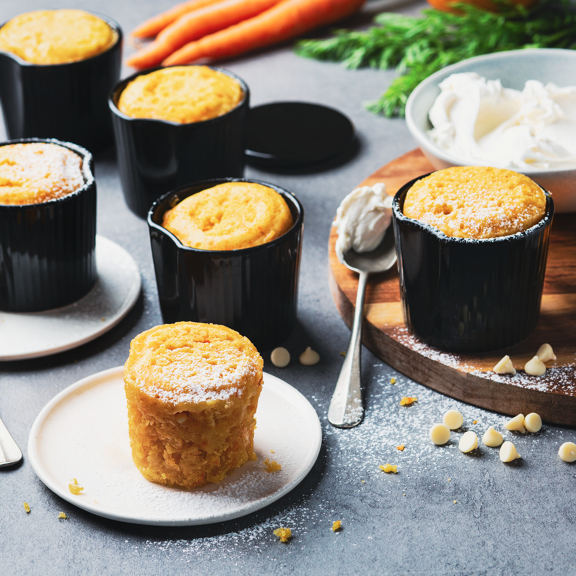 Tortine di carote singole in ramekin neri una servita su piattino bianco con formaggio spalmabile e gocce di cioccolato bianco