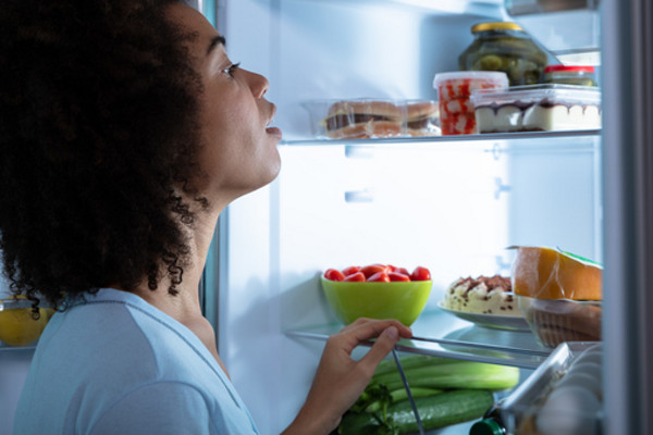 Side View Of Young African Woman Searching Food In An Open Refrigerator