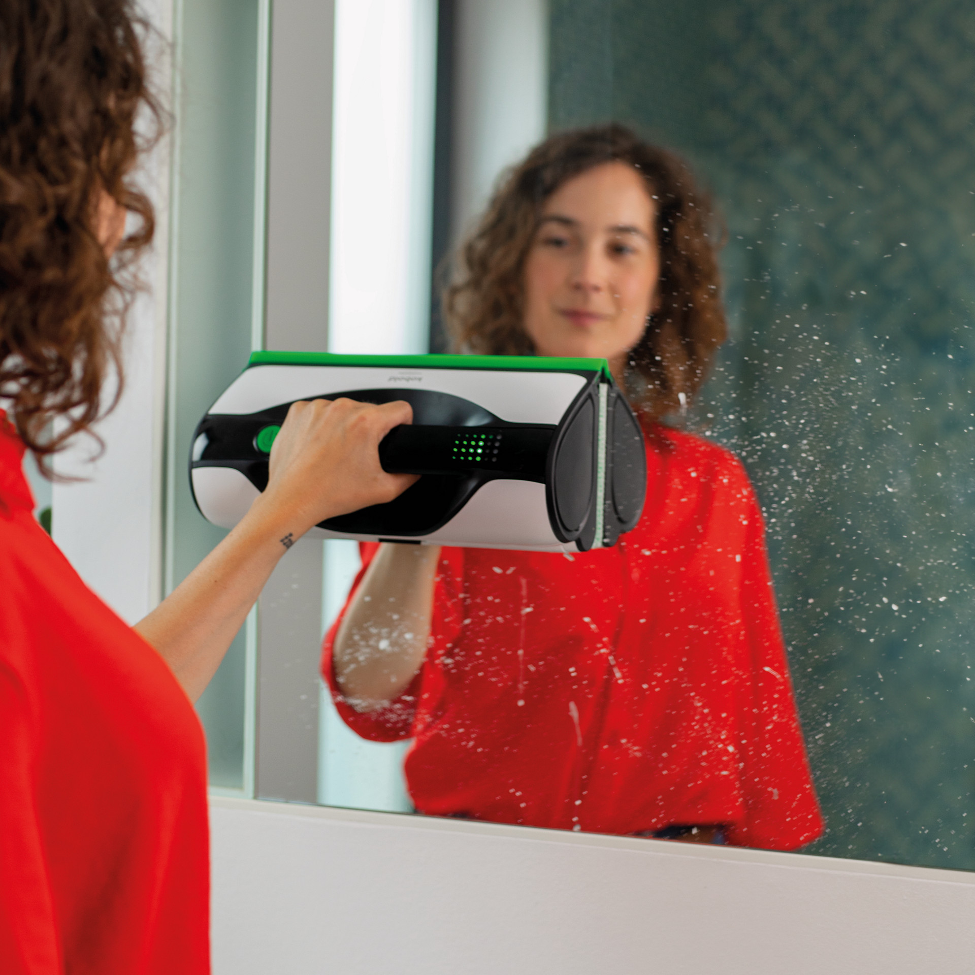 Personne utilisant le nettoyeur de vitres Kobold VG100+ sur un miroir de salle de bain.