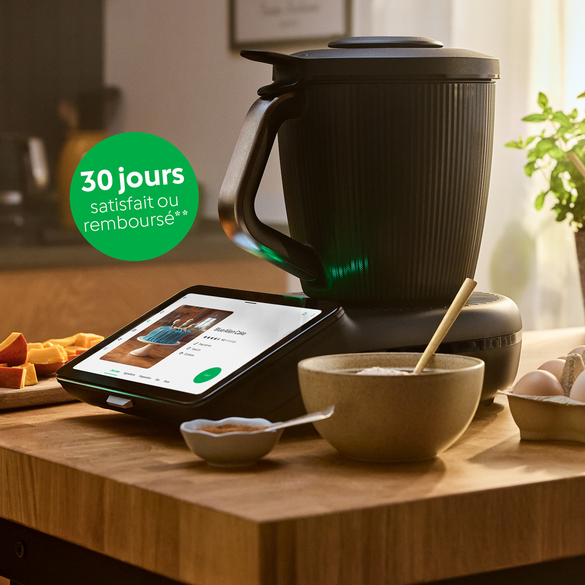 Thermomix® TM7 sur un plan de travail de cuisine avec ingrédients, herbes, ustensiles et œufs à la lumière du jour.