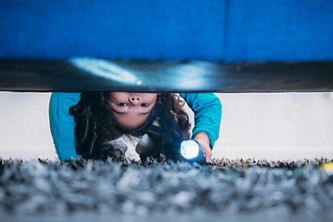 Une petite fille cherche quelque chose sous le lit dans une chambre.