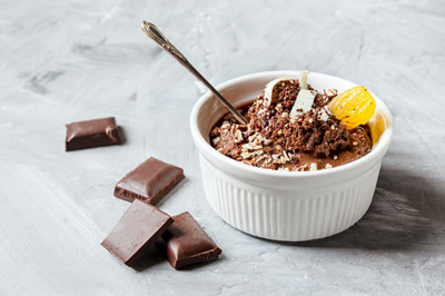 Mousse au chocolat garnie d'un quartier de mandarine et de copeaux de chocolat blanc dans un bol blanc et morceaux de chocolat sur une table grise