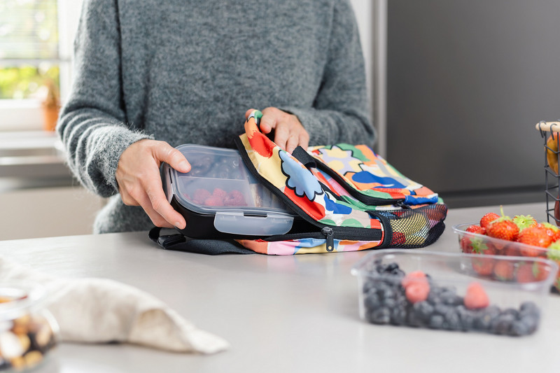 Dans la cuisine, une maman prépare une boîte à lunch avec des collations dans un sac à dos d'écolier.