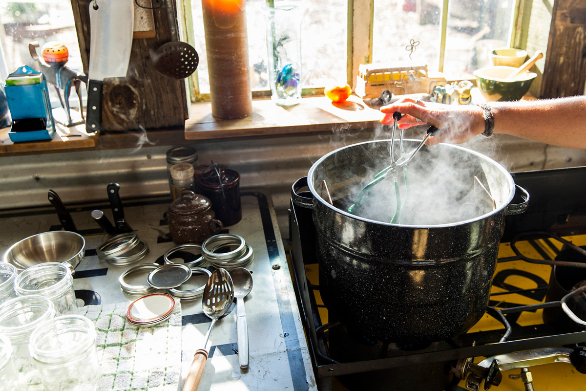 Woman using tongs to remove preserves jar from steaming saucepan