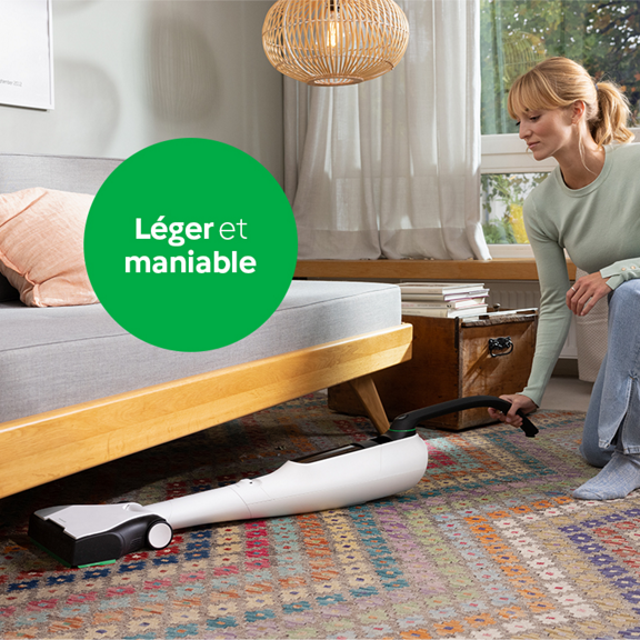 Femme nettoyant sous un canapé avec l aspirateur sans fil Kobold VK7 illustrant sa légèreté et maniabilité