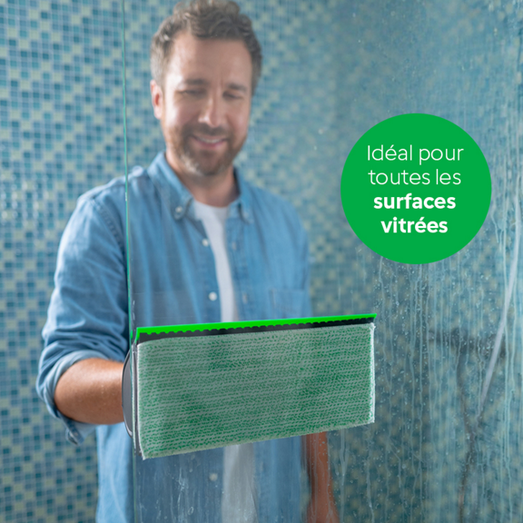 Personne nettoie une vitre avec le nettoyeur de vitres Kobold VG100 dans une salle de bain texte souligne usage vitres