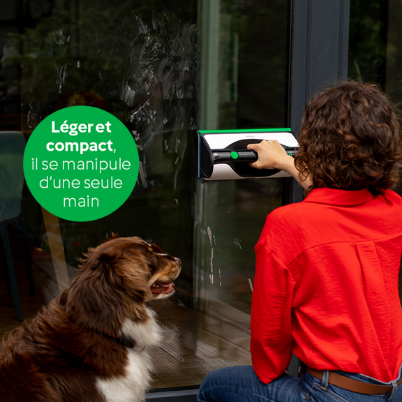 Personne nettoyant une porte vitrée avec le nettoyeur de vitres Kobold VG100 chien assis à côté bulle de texte verte