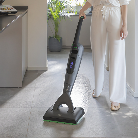 Personne nettoie le sol carrelé dans une cuisine avec aspirateur laveur sans fil Kobold VK7 avec brosse DuoSpeed SP7 produit et jambes visibles