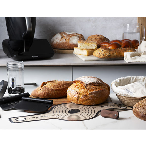 Thermomix TM7 avec pains cuits ustensiles de découpe et accessoires à pain sur un plan de travail
