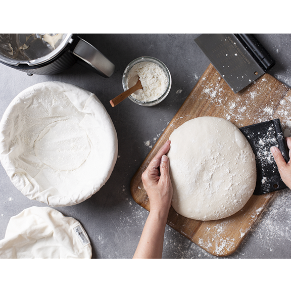 Mains façonnant une pâte sur une planche avec Thermomix TM7 bol pot de farine et raclette