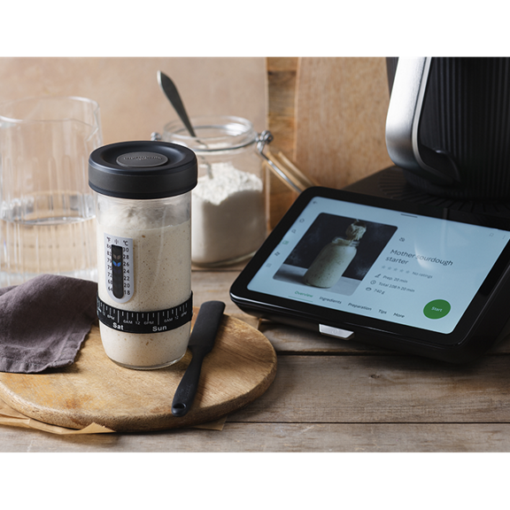 Thermomix TM7 à côté d un bocal de levain écran affichant la recette farine et ustensiles de pâtisserie
