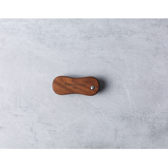 Poignée en bois Thermomix avec logo gravé sur surface claire texturée