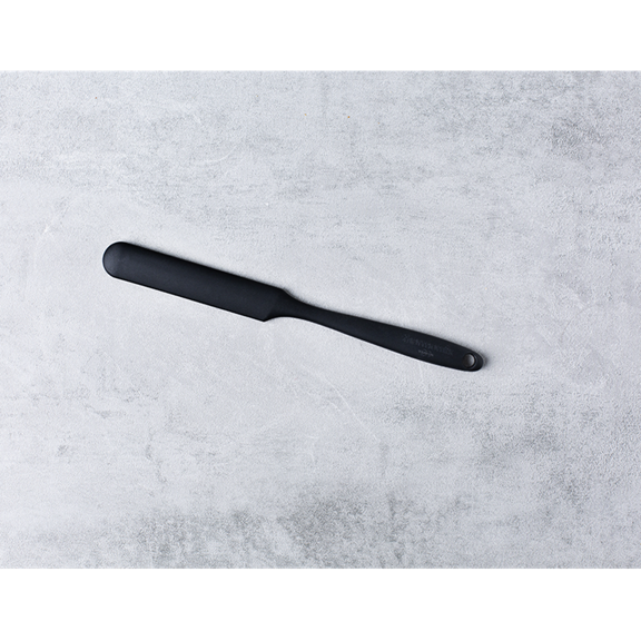 Spatule noire de cuisine sur surface gris clair manche orienté à droite