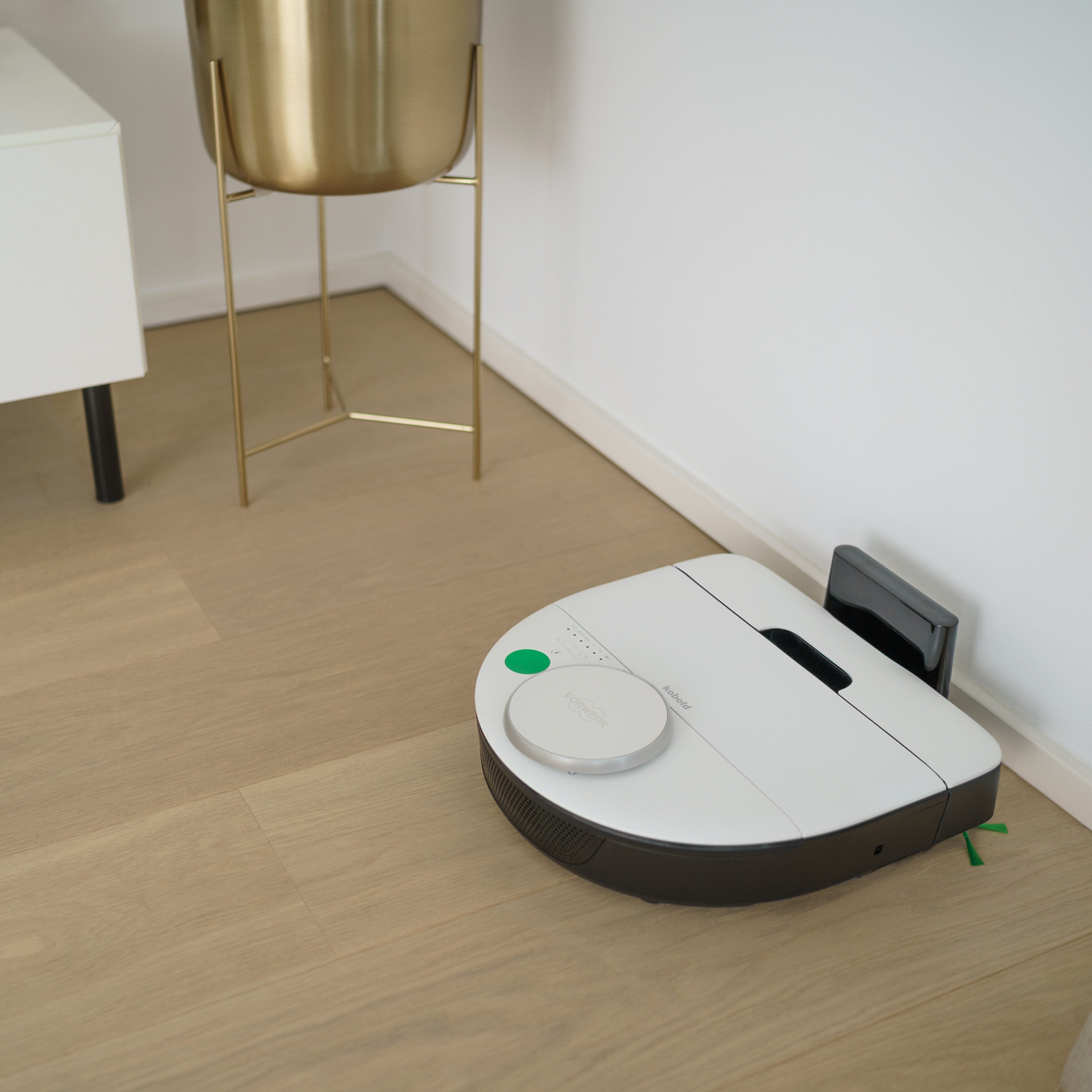 Robot aspirateur VR7 retourne vers sa station de charge dans un salon moderne avec sol en bois clair.