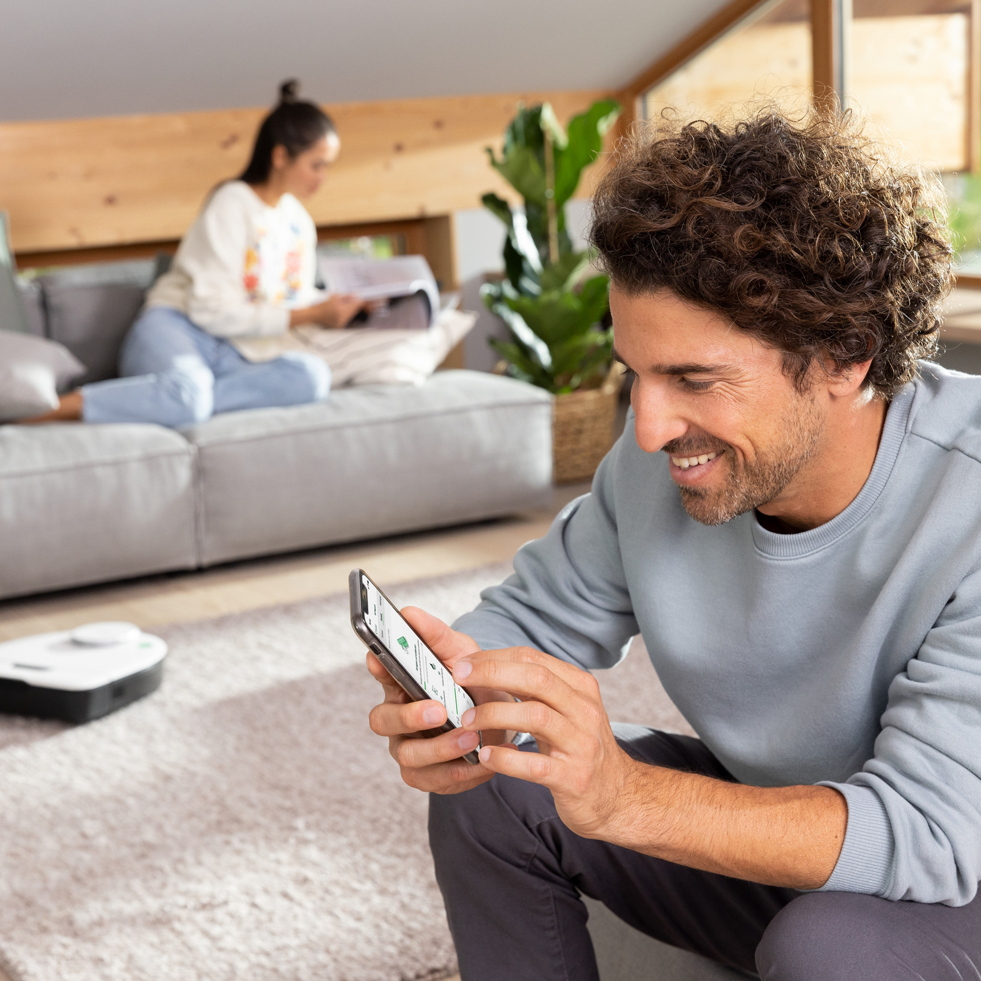 Personne utilise un smartphone pour contrôler le robot aspirateur VR7 dans un salon moderne.