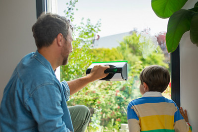 Un père de famille passe le nettoyeur de vitres VG100+ sur une vitre avec son fils à côté