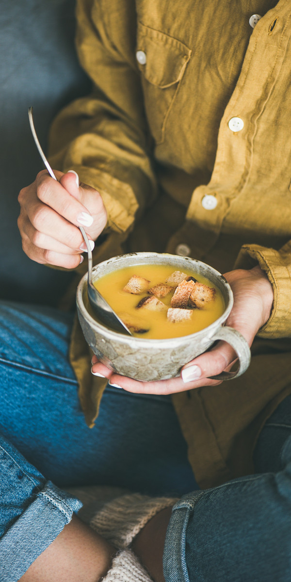 Femme assise en tailleur avec un bol de soupe à la main