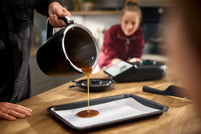 Une personne verse du caramel réalisé au Thermomix sur une plaque de cuisson recouverte de papier sulfurisé. 