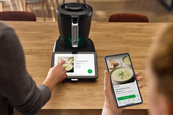 Une femme utilise le Thermomix TM7 et on voit l'écran du robot donnant sur une recette de soupe qu'on retrouve sur la plateforme Cookidoo 