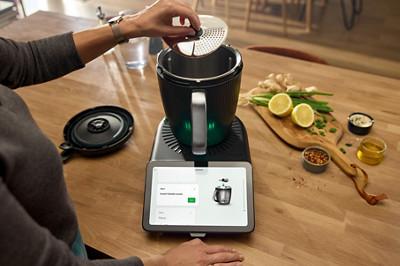 Une femme suit une recette et installe le couvre-lame éplucheur à l'intérieur du robot thermomix allumé. 