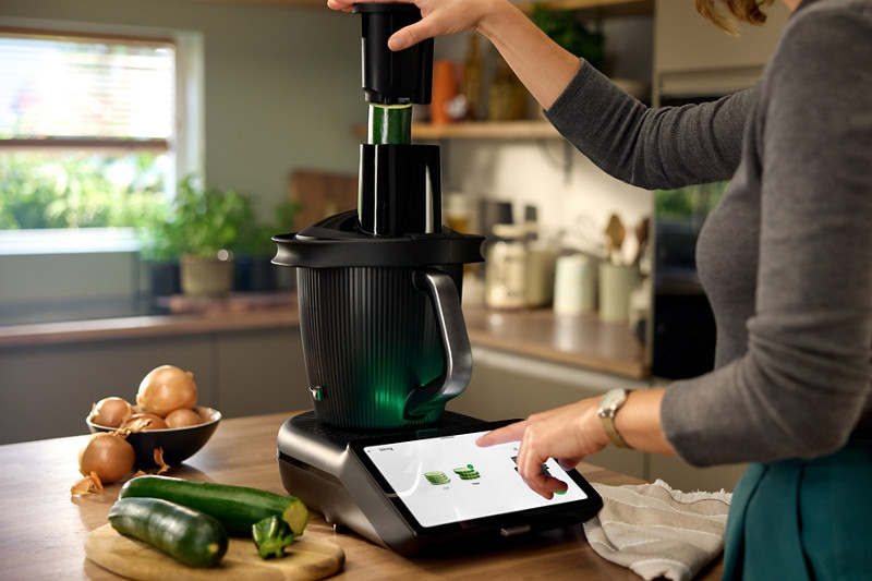 Une femme utilise le Thermomix en insérant des courgettes dans le découpe-minute. 