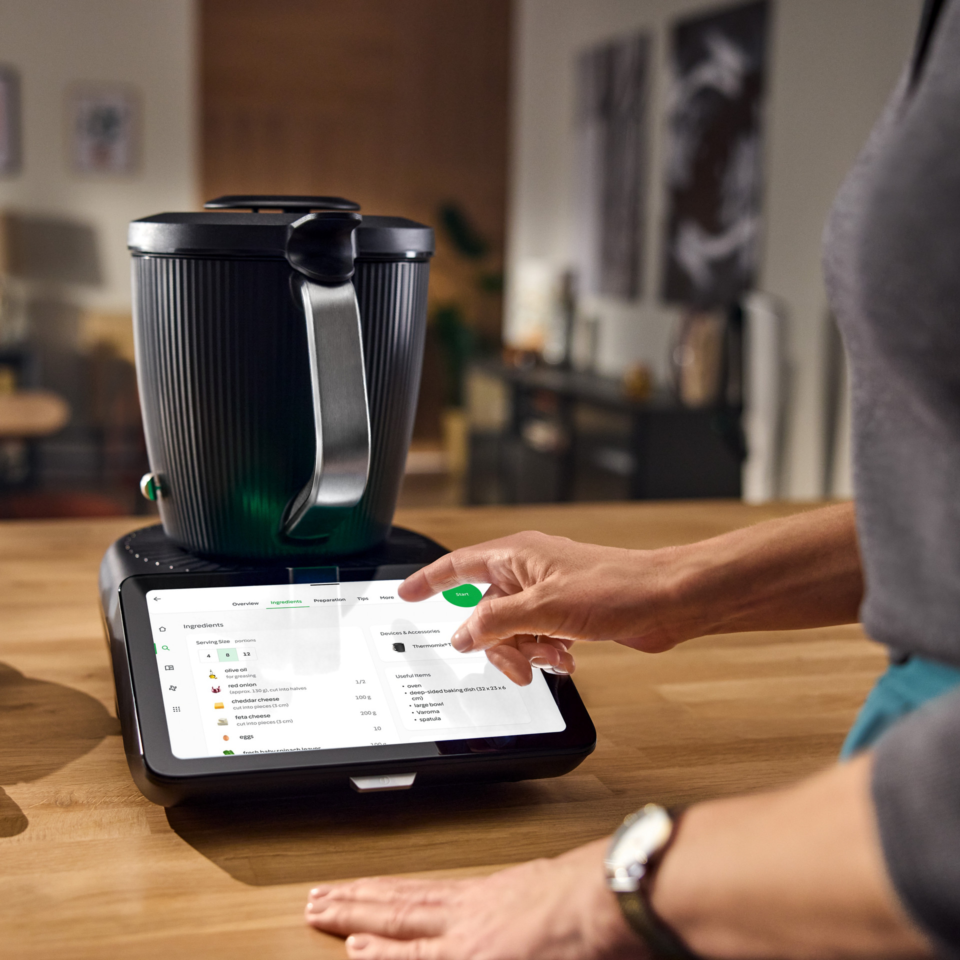 Personne sélectionne une recette sur l'écran tactile du Thermomix® TM7, bol de pommes de terre à côté.