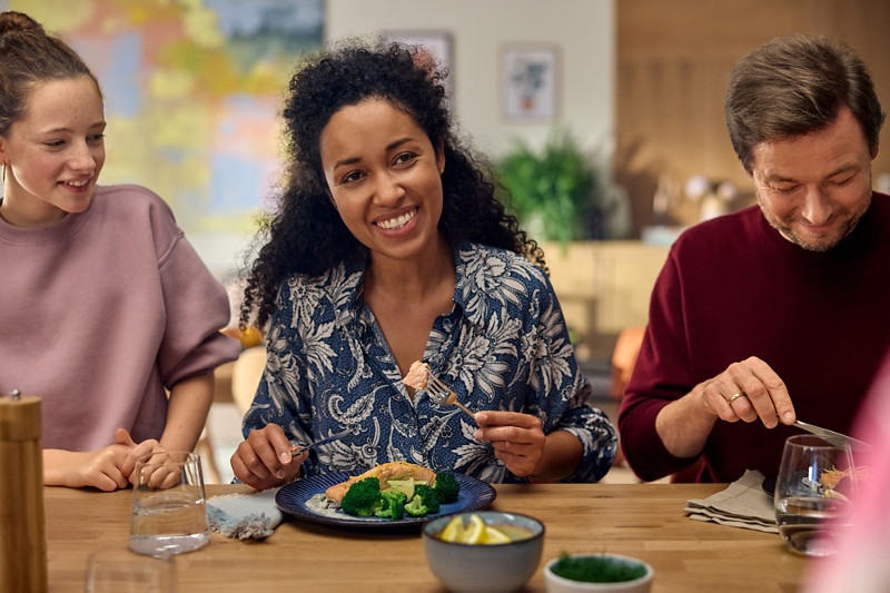 Trois amis mangent un plat préparé au Varoma du Thermomix, du saumon avec des brocolis. 
