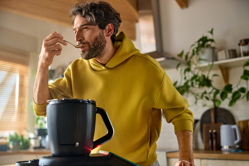 Un homme goûte le plat qu'il vient de réaliser au Thermomix. Le robot est placé devant lui, sur le plan de travail.