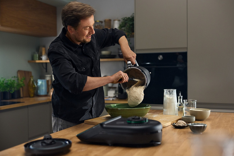 Un homme verse sa pâte à pain réalisé au Thermomix, dans un saladier, à l'aide de la spatule. 