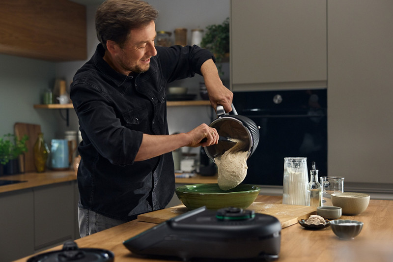 Un homme verse sa pâte à pain réalisé au Thermomix, dans un saladier, à l'aide de la spatule. 