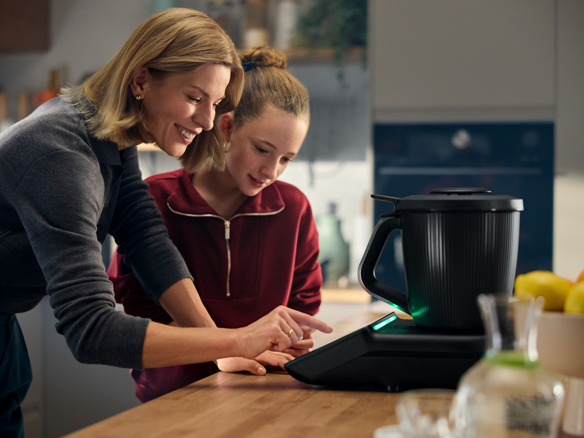 Deux personnes utilisent un Thermomix® TM7 sur un plan de travail, focalisées sur l’écran tactile de l’appareil.