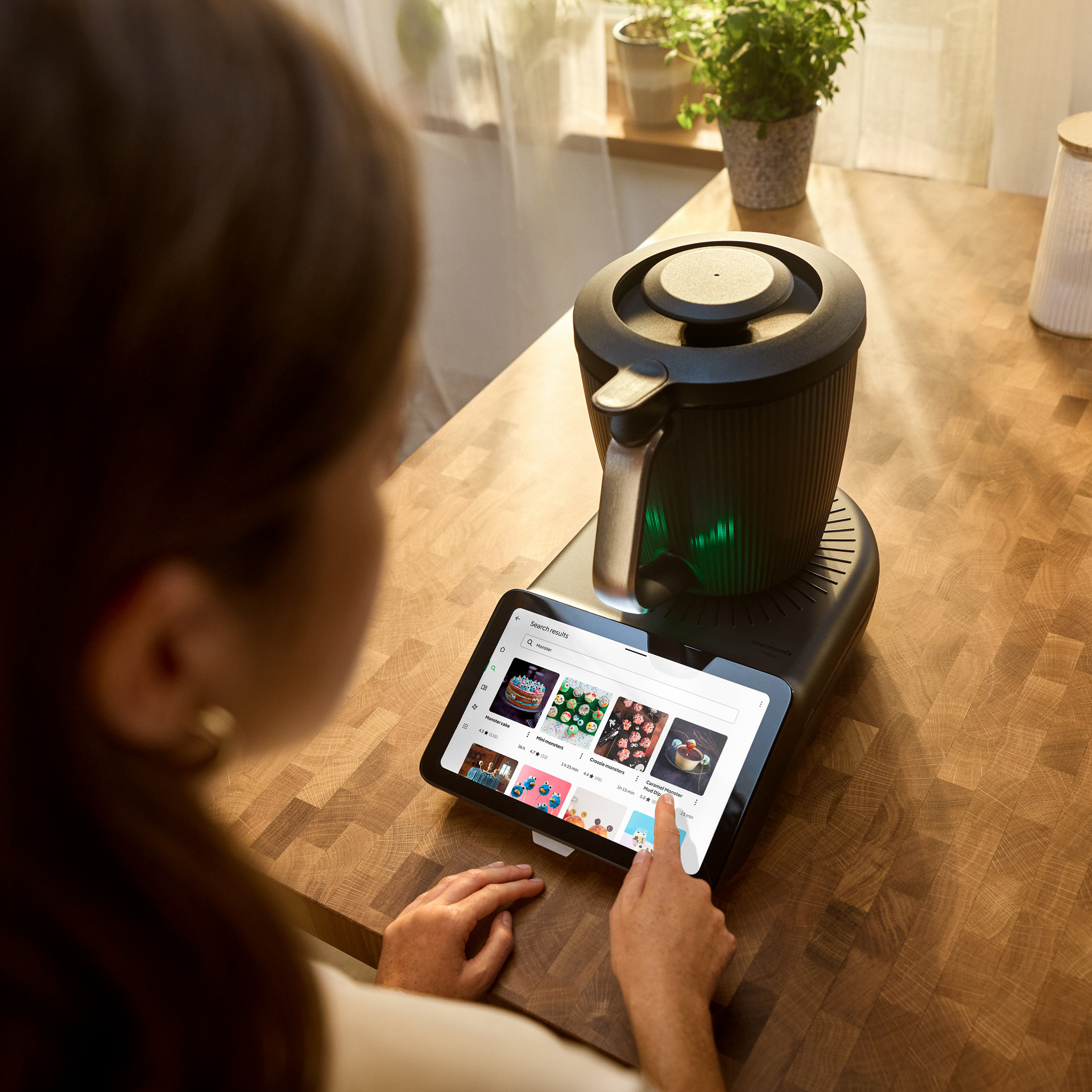 Personne utilisant le Thermomix® TM7 sur un plan de travail en bois avec l’écran affichant des recettes.