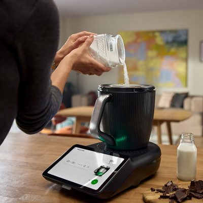 Une femme verse du sucre dans le bol du Thermomix pour faire de la patisserie. 