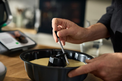 Une personne installe le Thermomix Sensor, la sonde de température Thermomix, dans un gâteau.