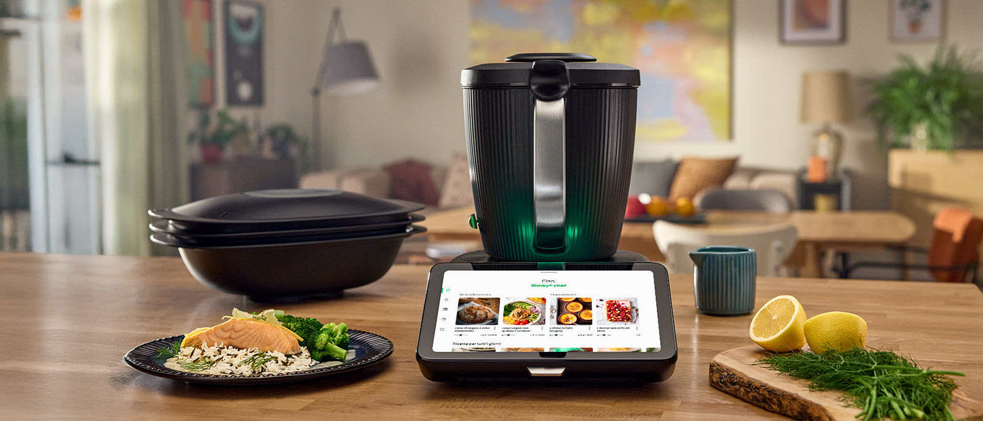 Bimby TM7 su piano cucina con piatto, limone, erbe e accessori Varoma in ambiente moderno.