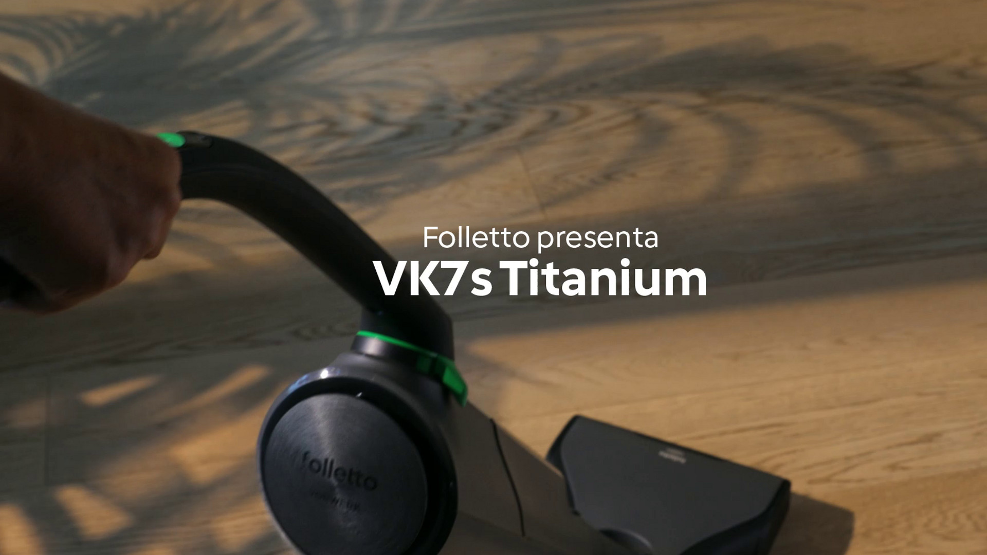 Mano che usa il sistema di pulizia Folletto VK7s su pavimento in legno, con testo sul prodotto.