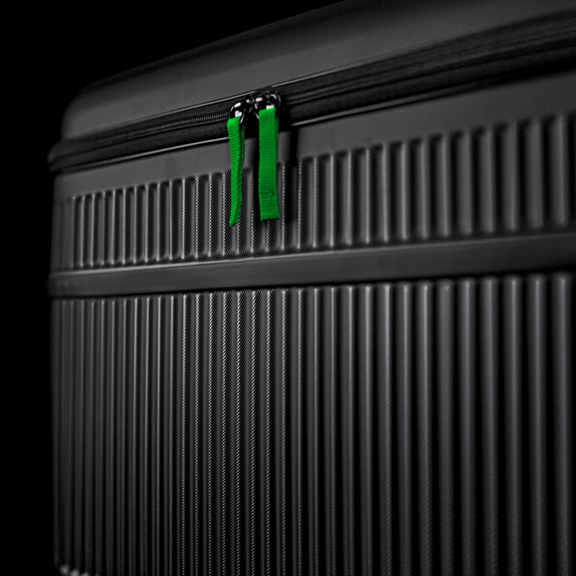 Black ribbed suitcase with green zipper pulls in close up against a dark background