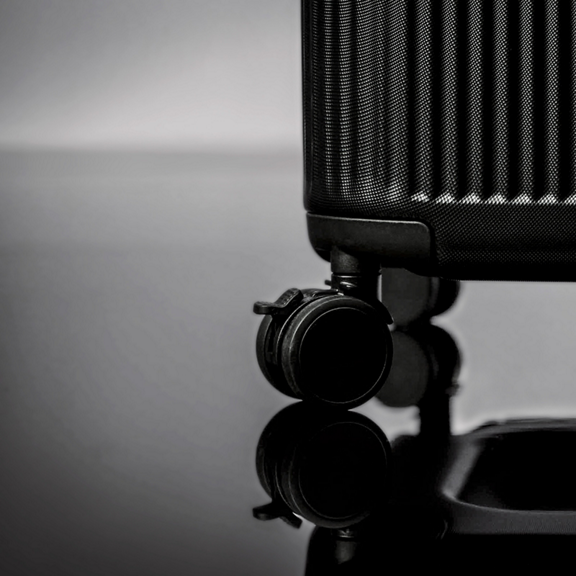 Close up of a hard shell suitcase corner with two black wheels on a reflective surface
