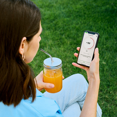 Woman with smartphone and smoothie sitting on bench in park