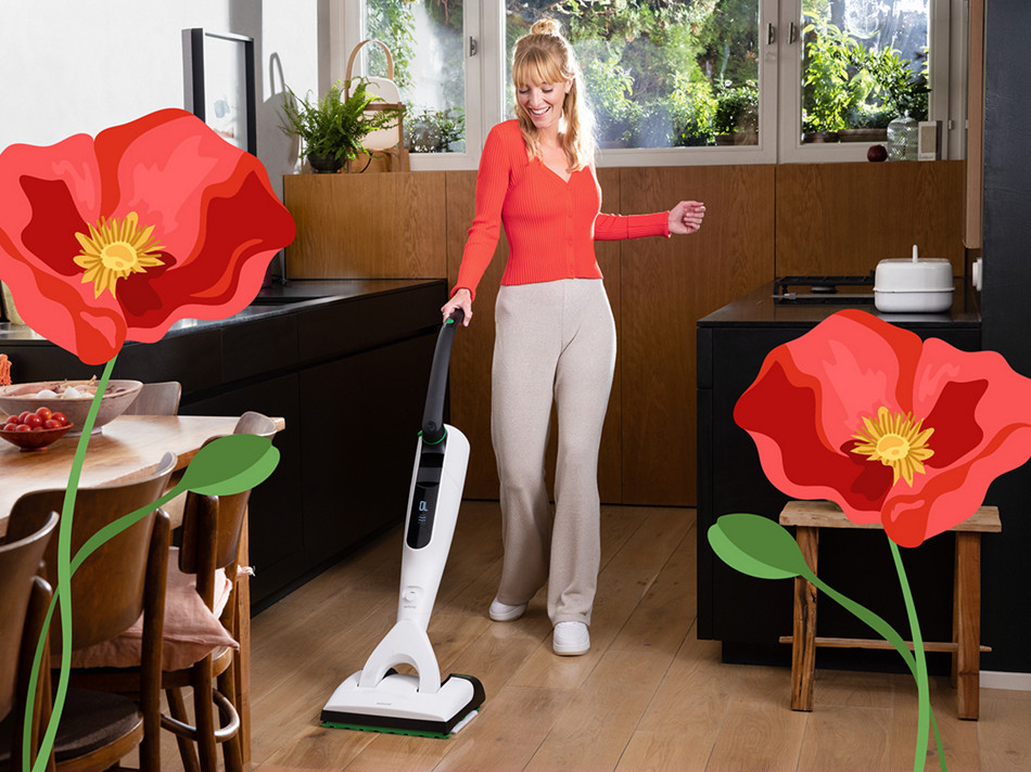 Person reinigt Küchenboden mit Kobold VK7 in heller Küche, große illustrierte rote Blumen im Vordergrund.