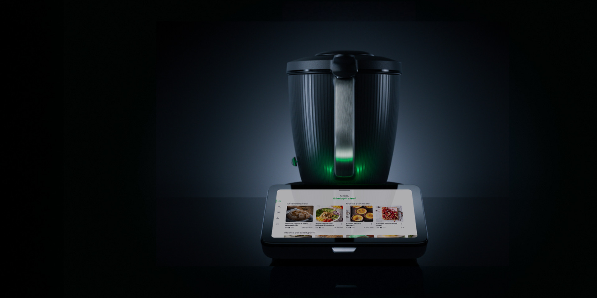 Bimby TM7 con boccale illuminato e display touch che mostra la selezione di ricette in un ambiente buio.