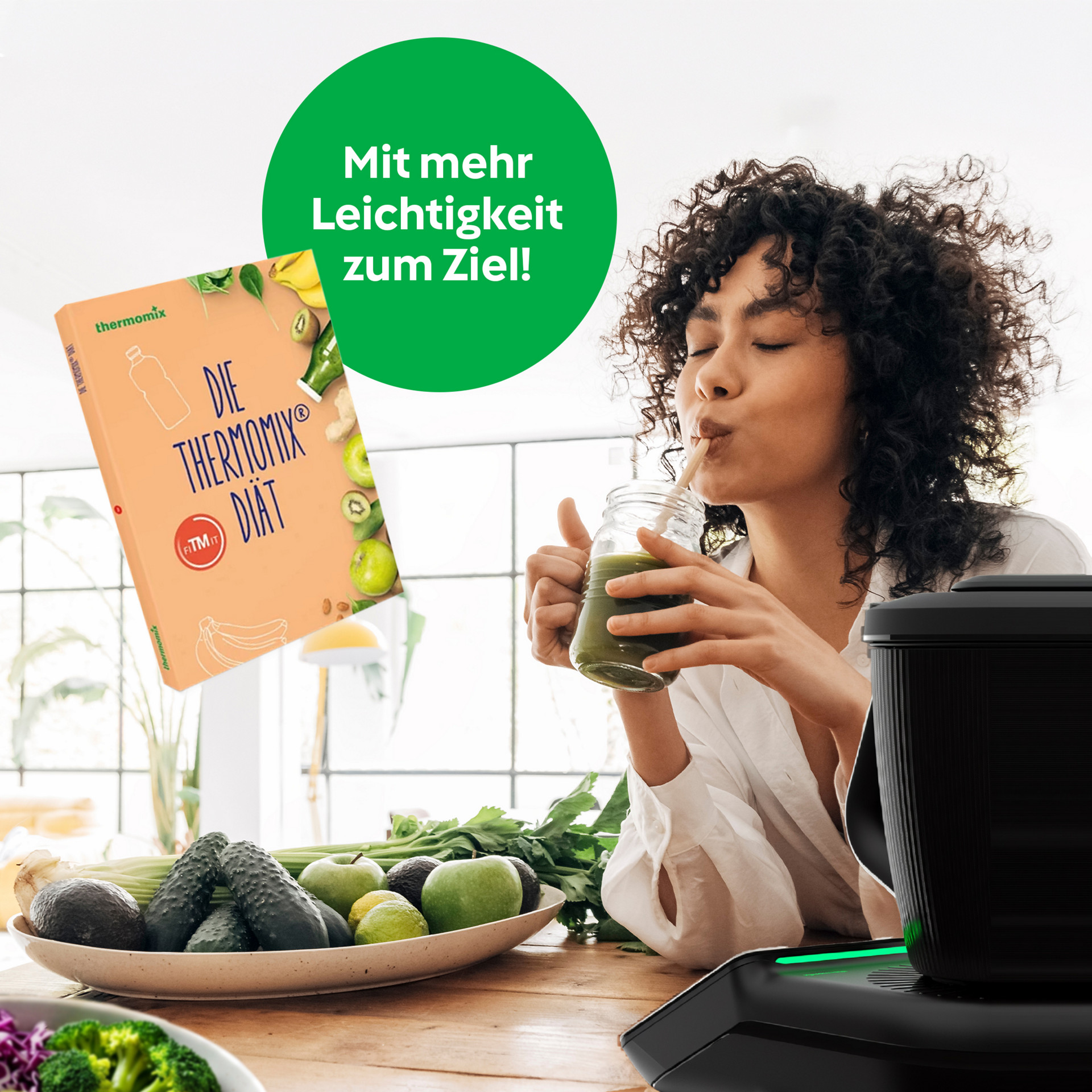 Frau trinkt einen grünen Smoothie am Tisch mit Obst und Gemüse, Thermomix® TM7 und „Die Thermomix® Diät“-Buch sichtbar.