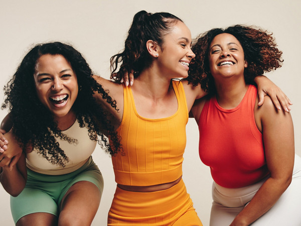 3 Frauen in Sportkleidung stehen lachend Arm in Arm