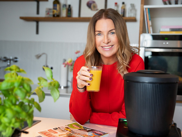 Frau neben Thermomix TM7 trinkt orangenen Smoothie