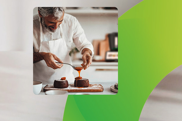 Koch bereitet ein Dessert in Küche zu, dahinter der Thermomix