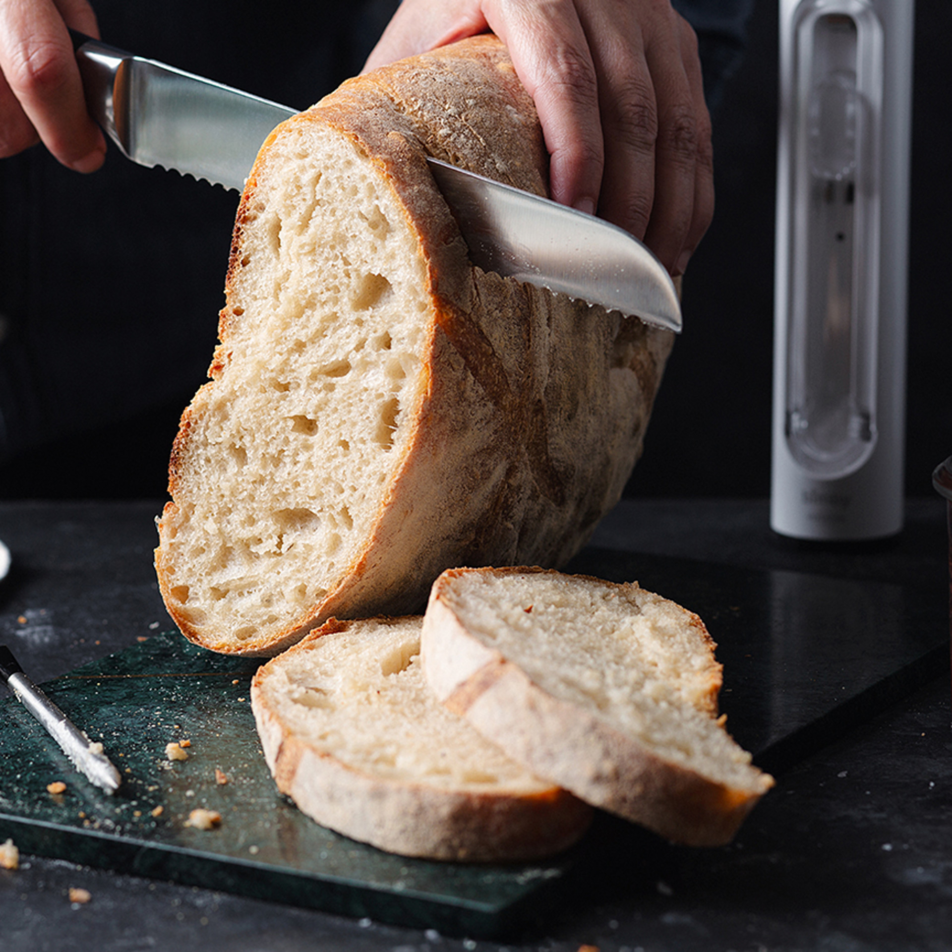 Frisches Brot wird auf einem Schneidebrett geschnitten, im Hintergrund steht ein Thermomix® Sensor aufrecht.
