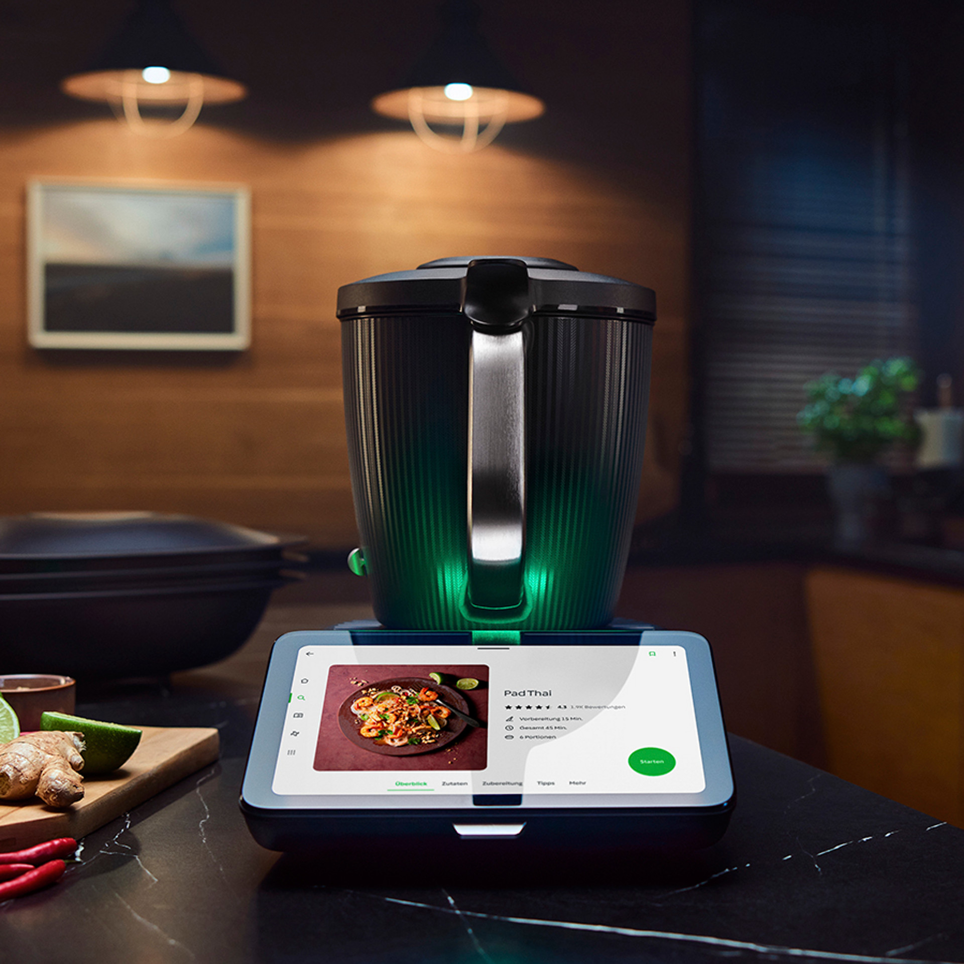 Thermomix® TM7 auf einer Küchenarbeitsplatte mit Rezeptanzeige, umgeben von frischen Zutaten in moderner Küche.