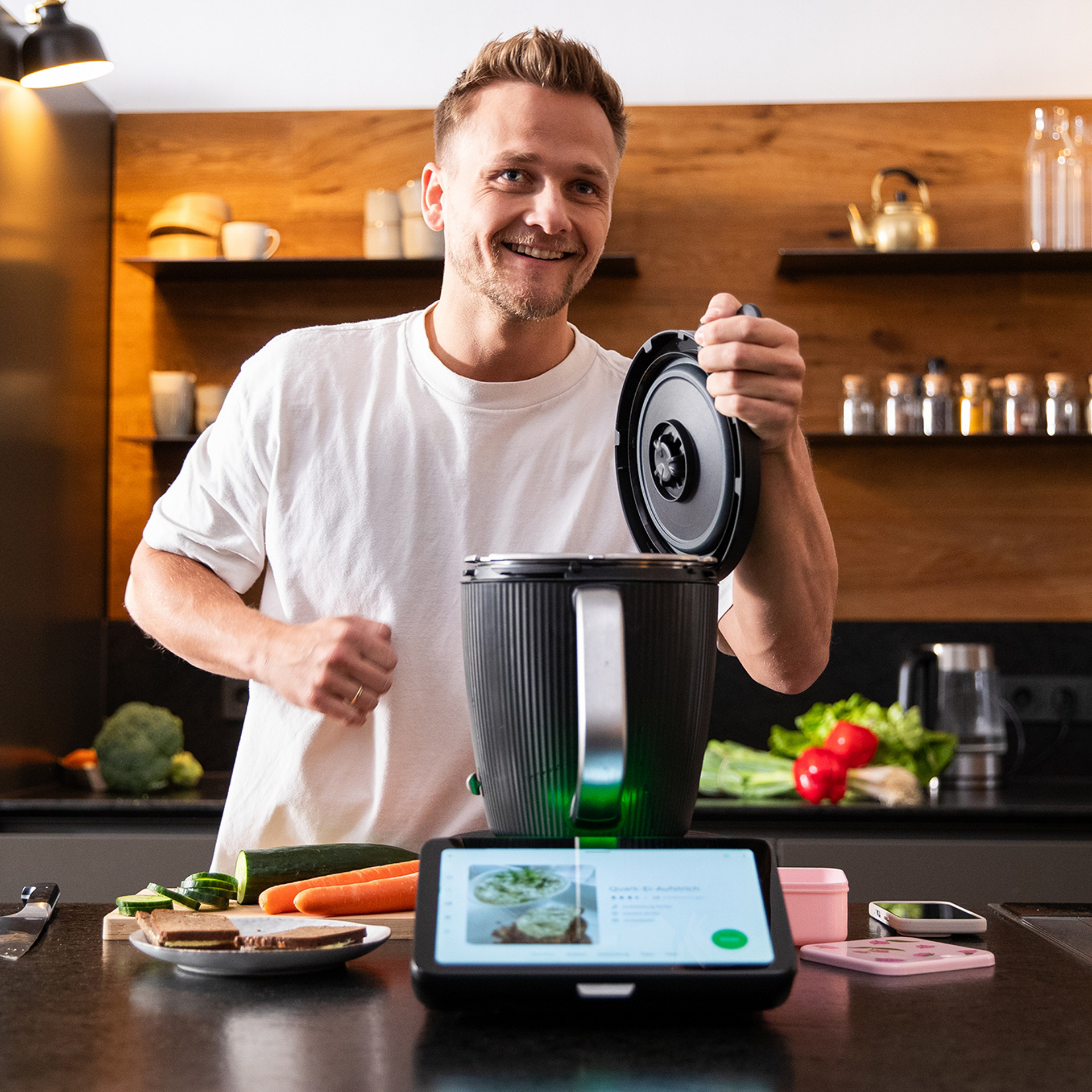 Person bereitet Gemüse in einer modernen Küche mit dem Thermomix® TM7 und Rezeptanzeige auf dem Display zu.