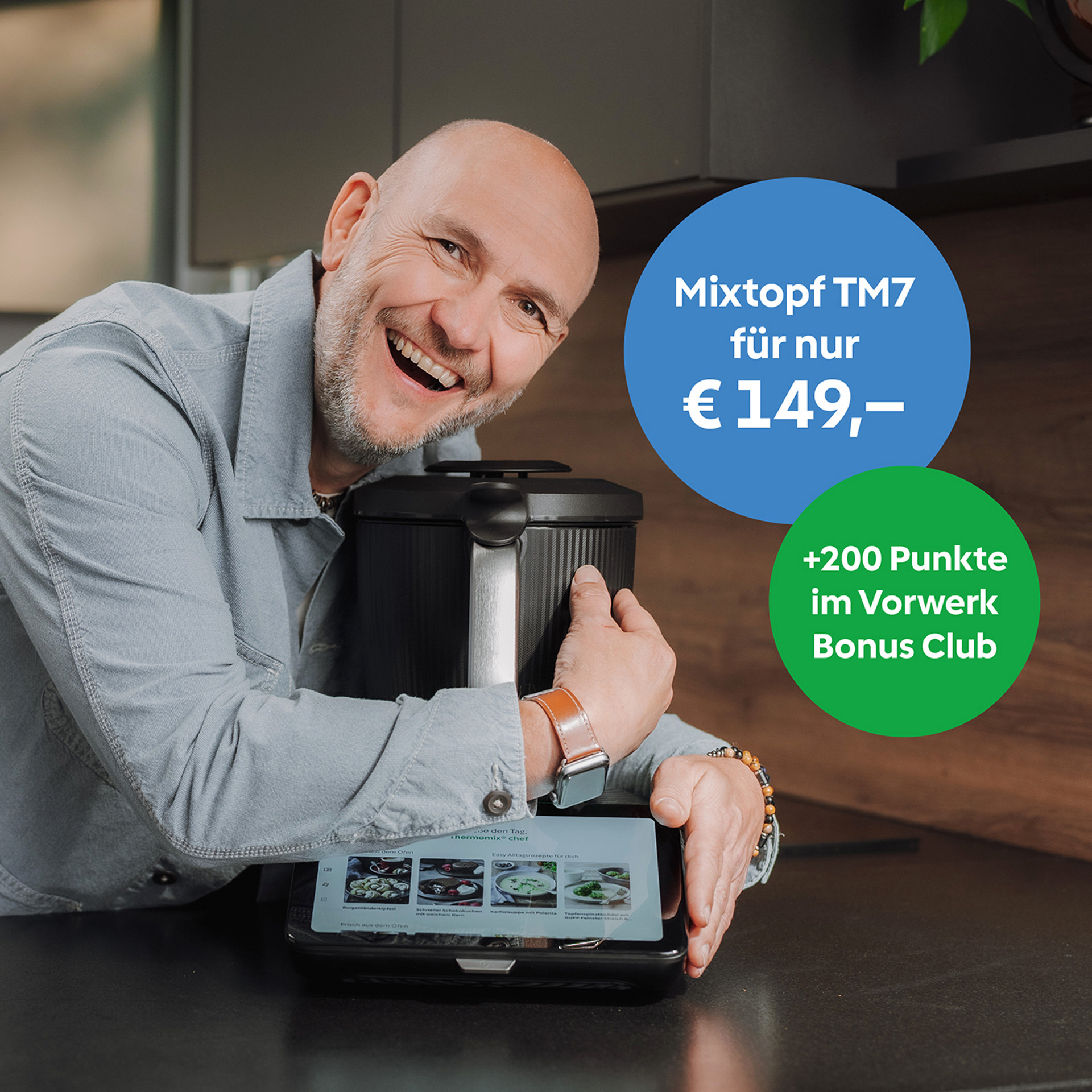 Lachender Mann umarmt Thermomix® TM7 in einer Küche, mit Bonus Club Angebot und Preisblasen auf Deutsch.